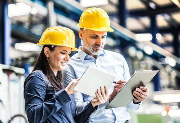 a man and woman wearing hardhats looking at tablet