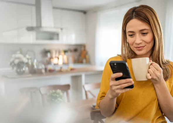 Eine Frau, die eine Tasse hält und auf ihr Handy schaut