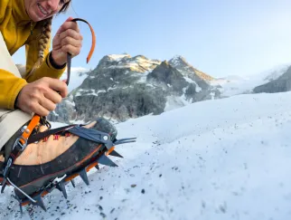 Eine Frau, die auf einem verschneiten Berg einen Schnürsenkel bindet.