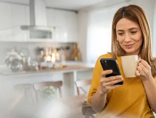 Eine Frau, die eine Tasse hält und auf ihr Handy schaut
