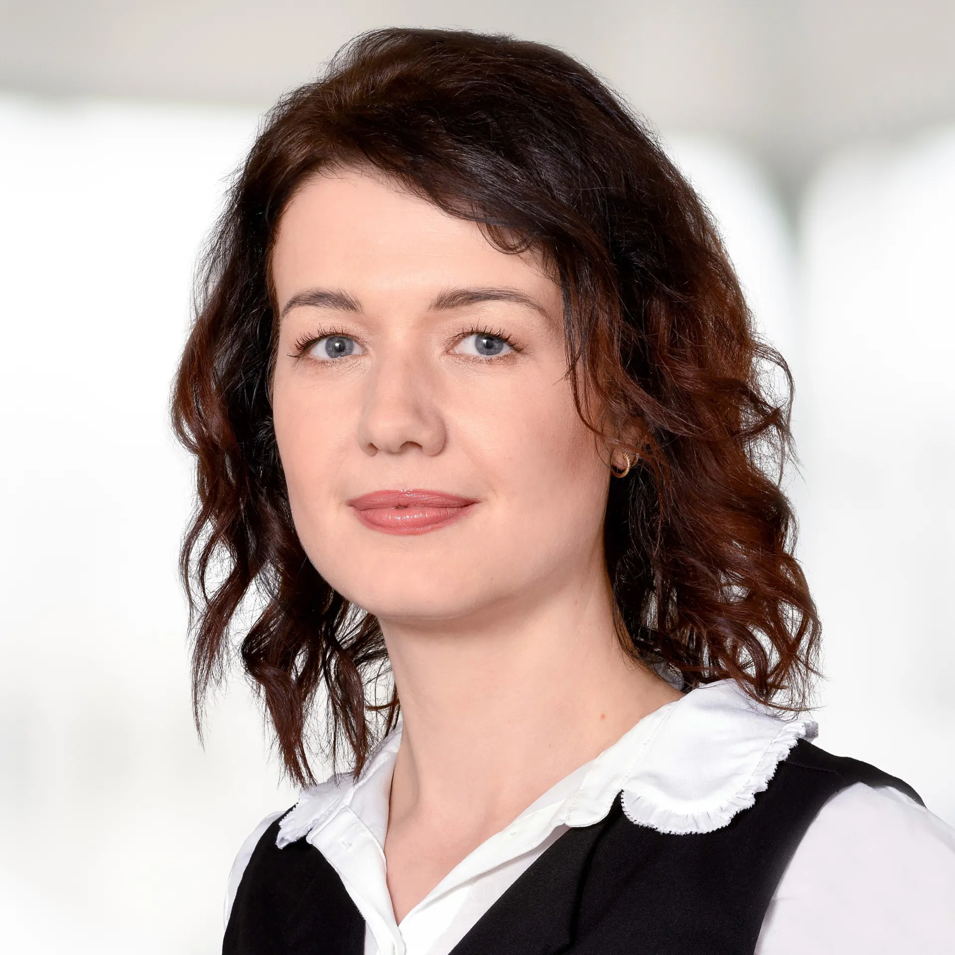 a woman with brown hair wearing a vest and white shirt